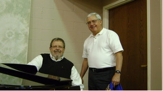 Two volunteers by a piano at Pancake Day in 2009