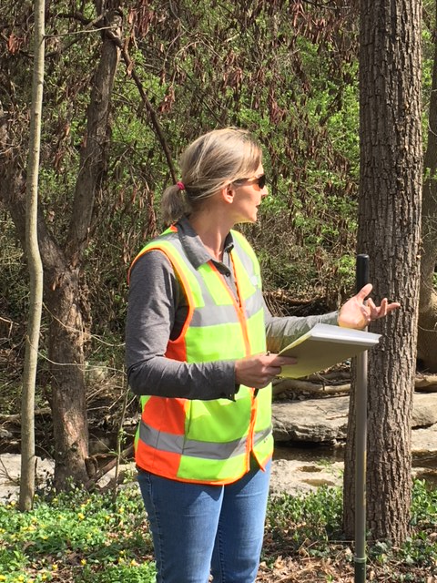Person in a reflective safety vest holding papers at the wooded planting site