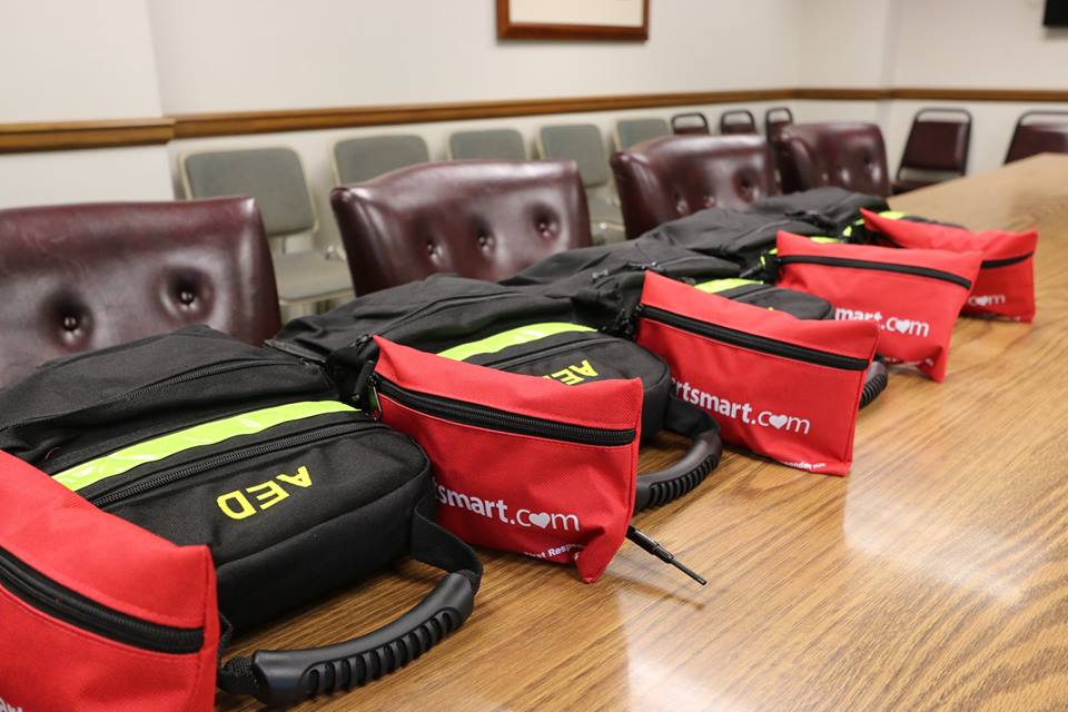Six AED cases and red supply bags arranged on a conference table
