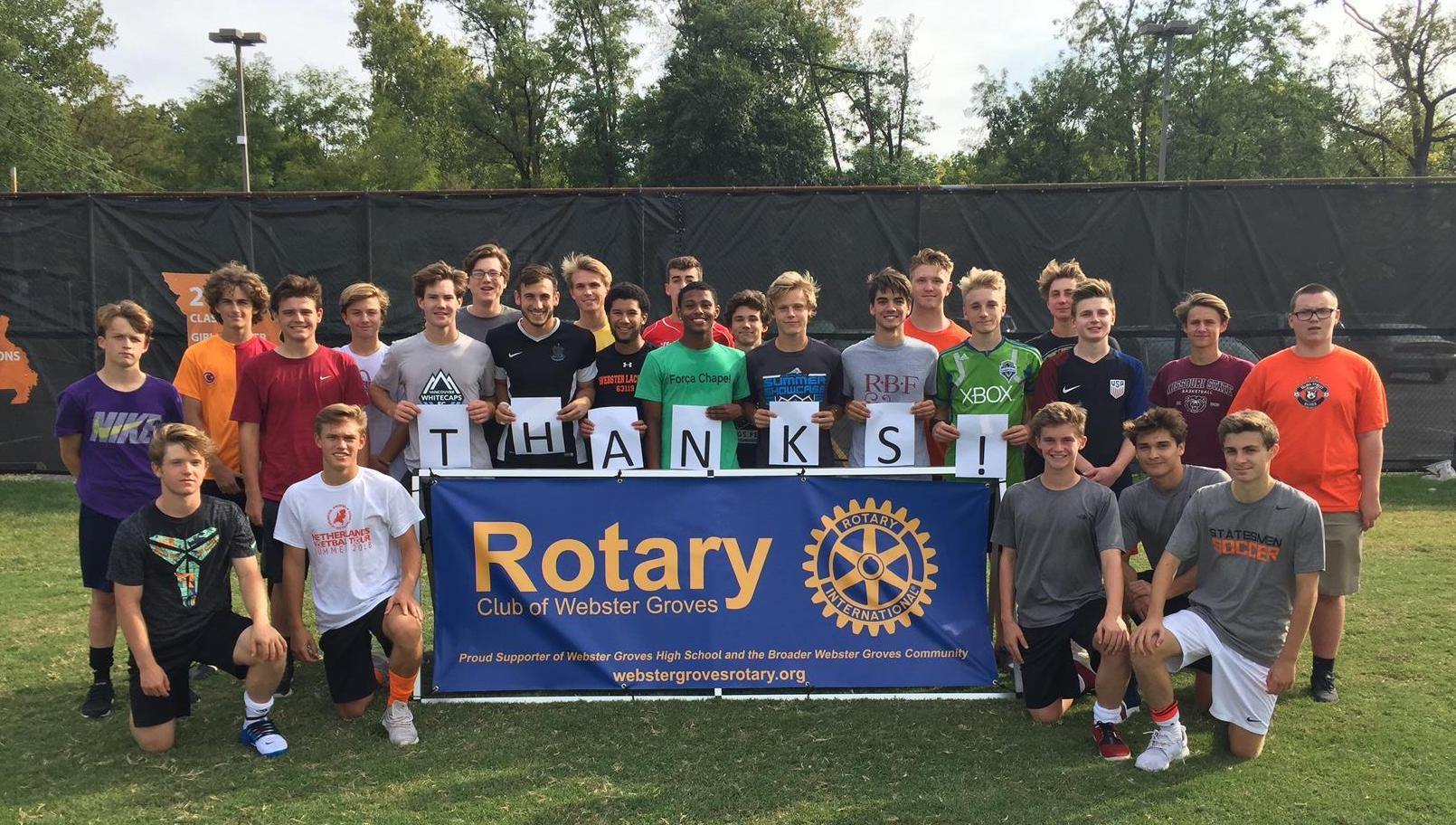 Webster Groves High School boys soccer team holding a thanks sign behind a Rotary Club of Webster Groves banner at the soccer field